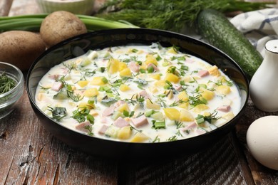 Photo of Delicious okroshka soup with kefir in bowl and ingredients on wooden table, closeup