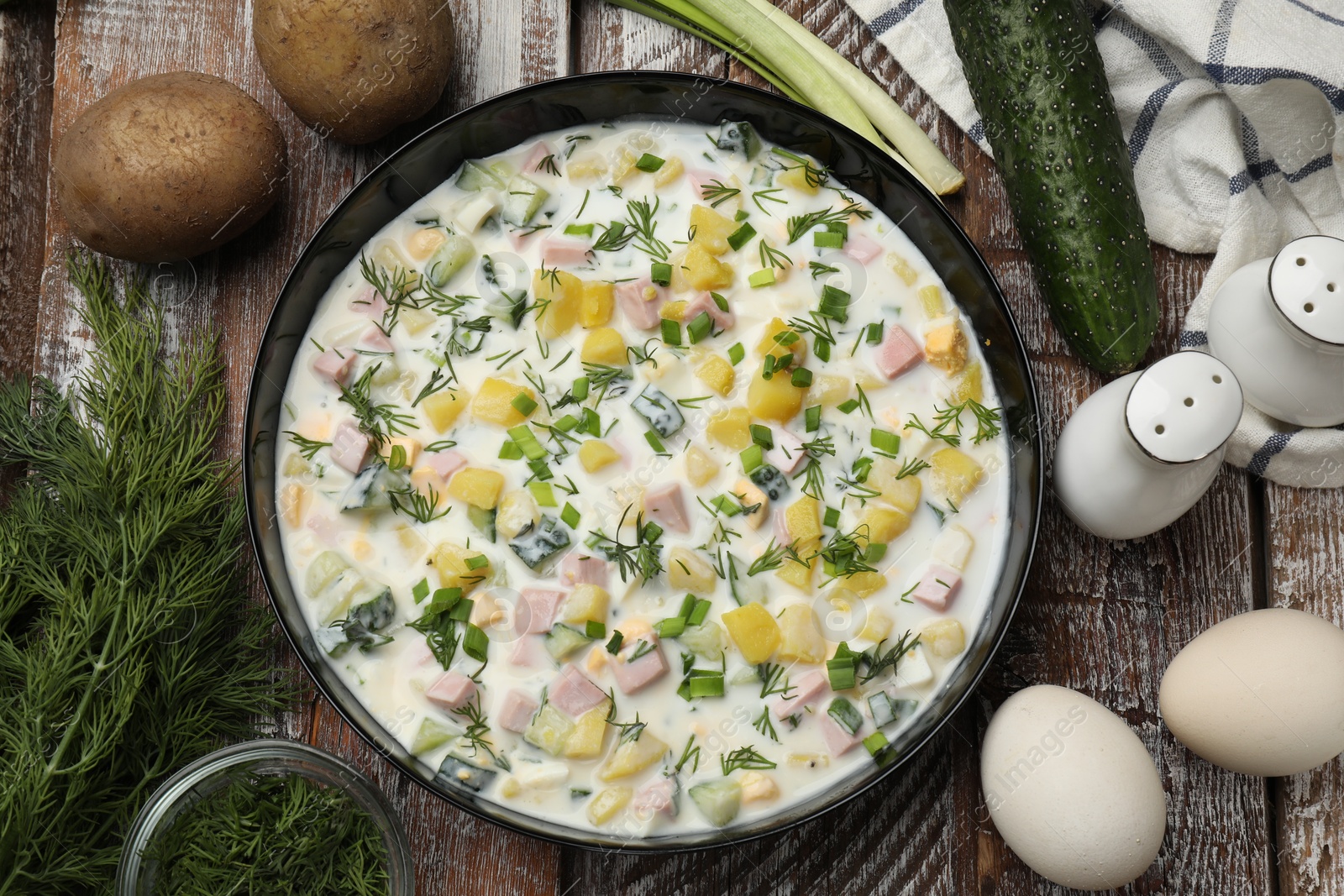 Photo of Delicious okroshka soup with kefir in bowl and ingredients on wooden table, flat lay