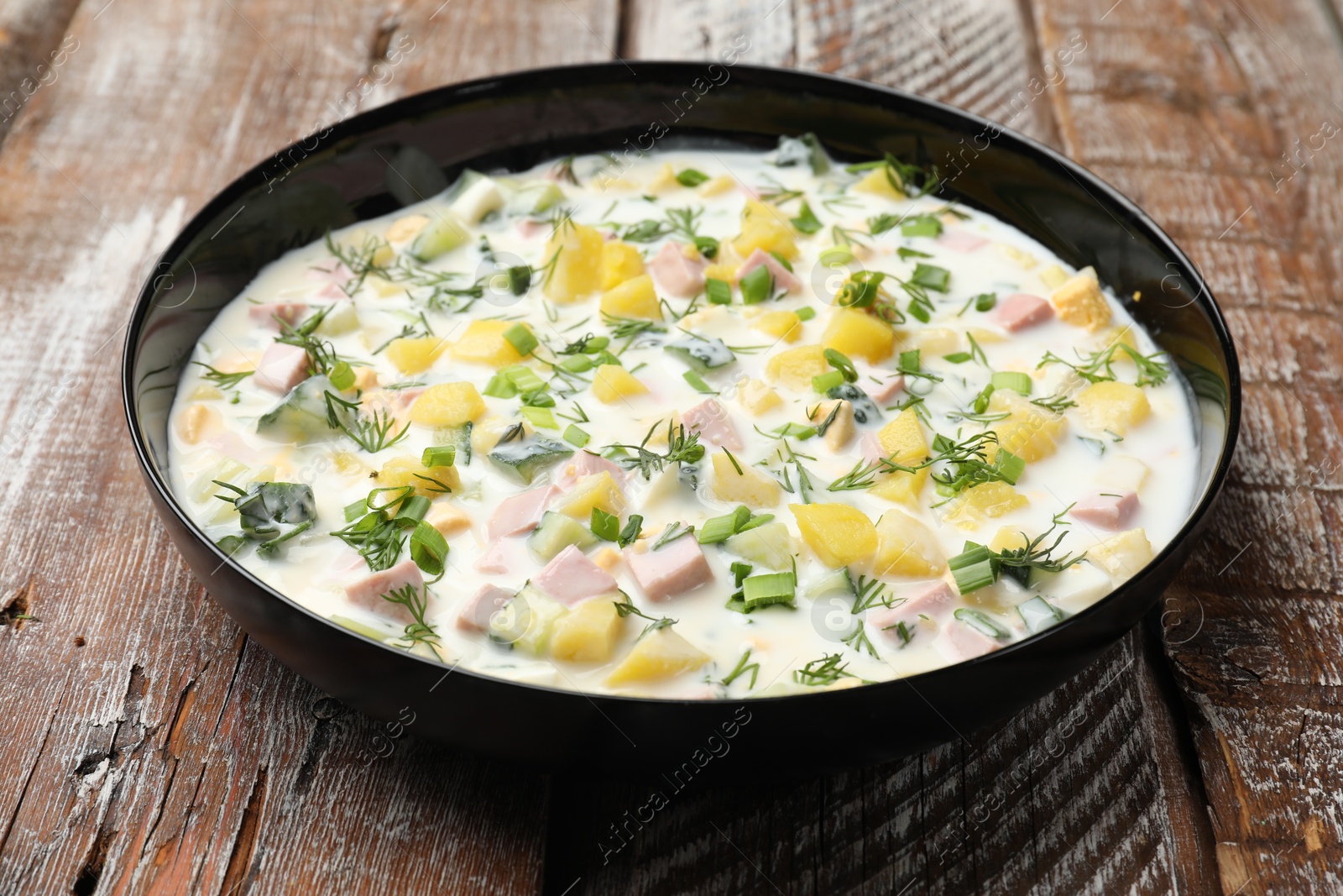 Photo of Delicious okroshka soup with kefir in bowl on wooden table, closeup