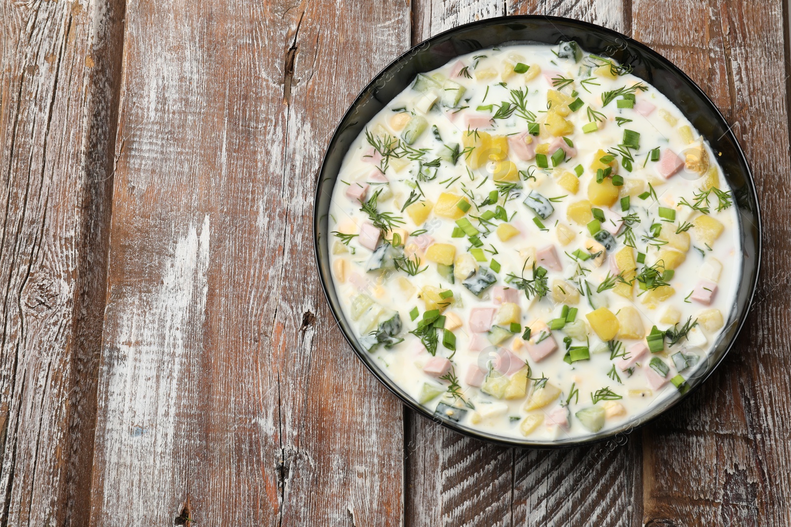 Photo of Delicious okroshka soup with kefir in bowl on wooden table, top view. Space for text