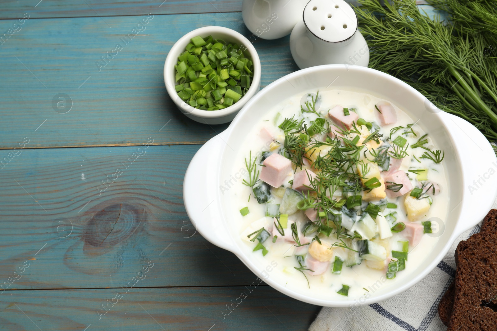 Photo of Delicious okroshka soup served on light blue wooden table, flat lay. Space for text