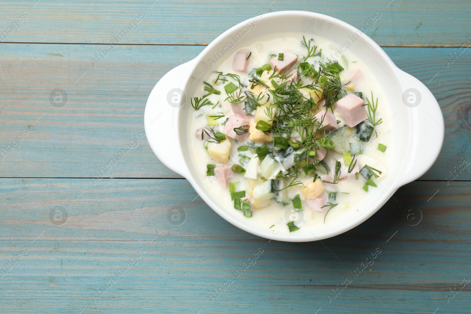 Photo of Delicious okroshka soup in bowl on light blue wooden table, top view. Space for text