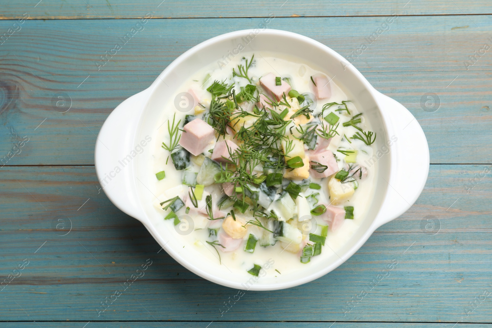 Photo of Delicious okroshka soup in bowl on light blue wooden table, top view