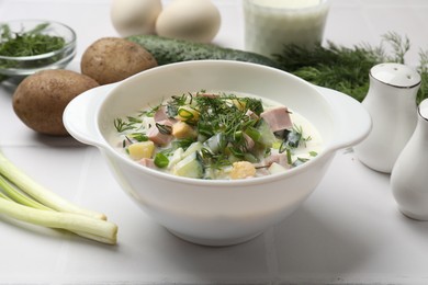 Photo of Delicious okroshka soup in bowl and ingredients on white table, closeup