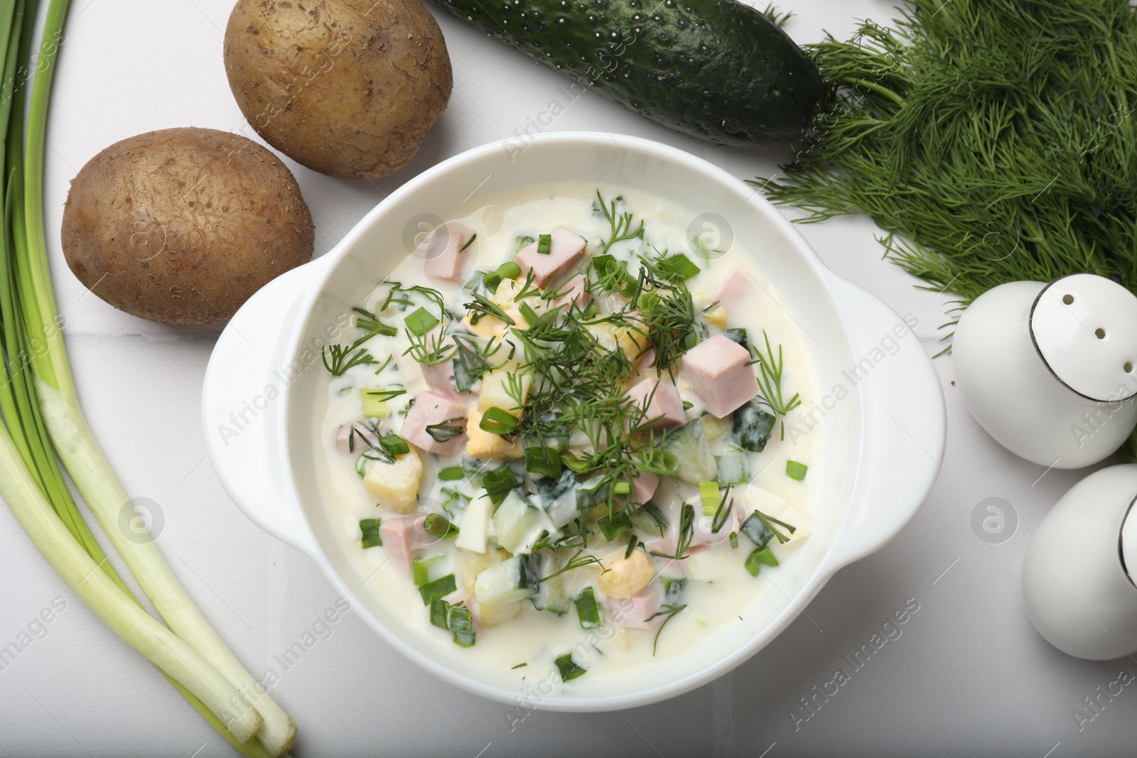 Photo of Delicious okroshka soup in bowl and ingredients on white table, flat lay