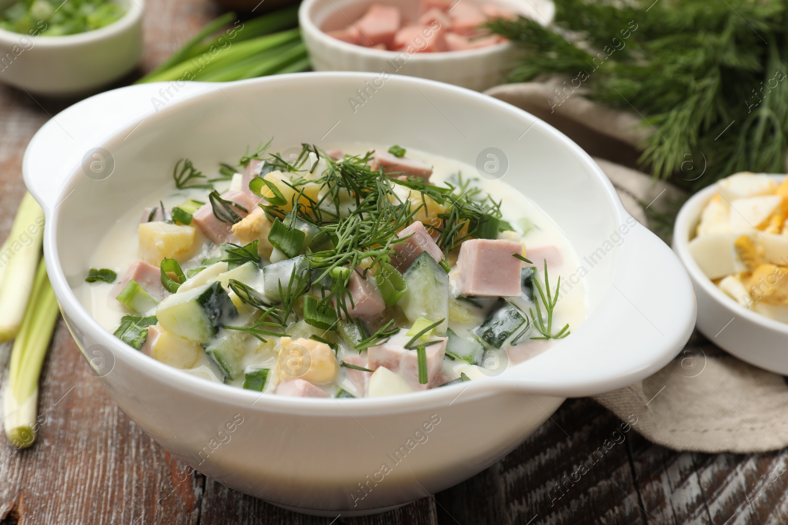 Photo of Delicious okroshka soup in bowl and ingredients on wooden table, closeup