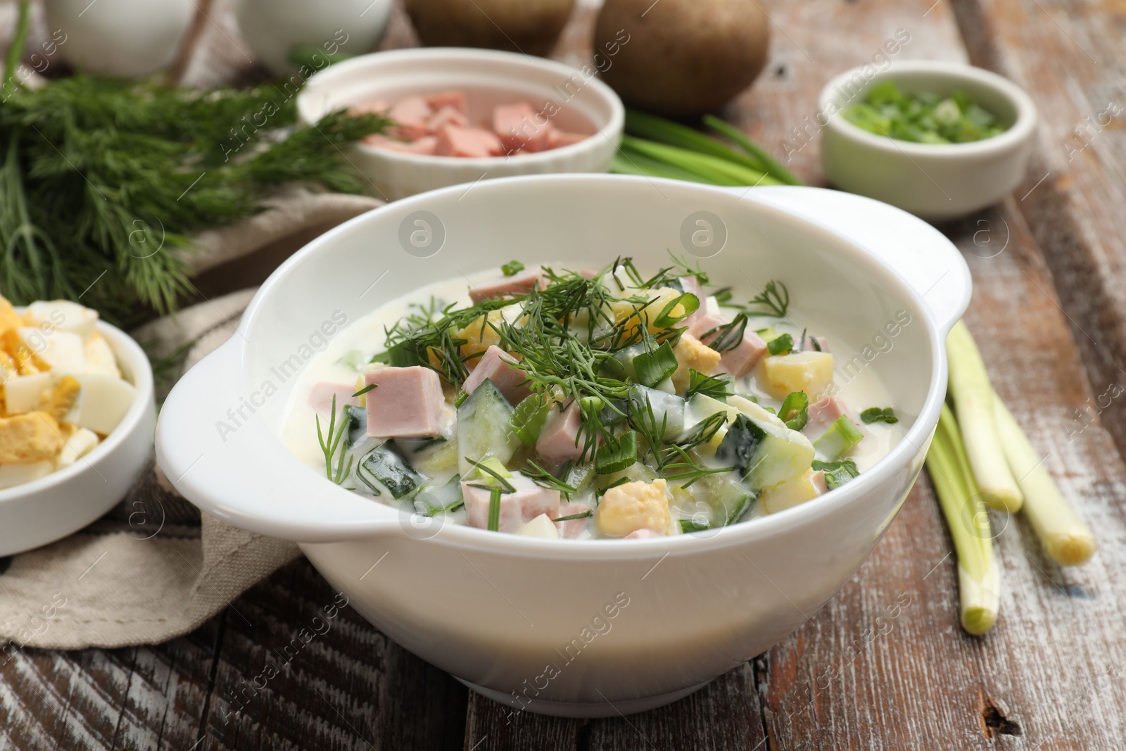 Photo of Delicious okroshka soup in bowl and ingredients on wooden table, closeup