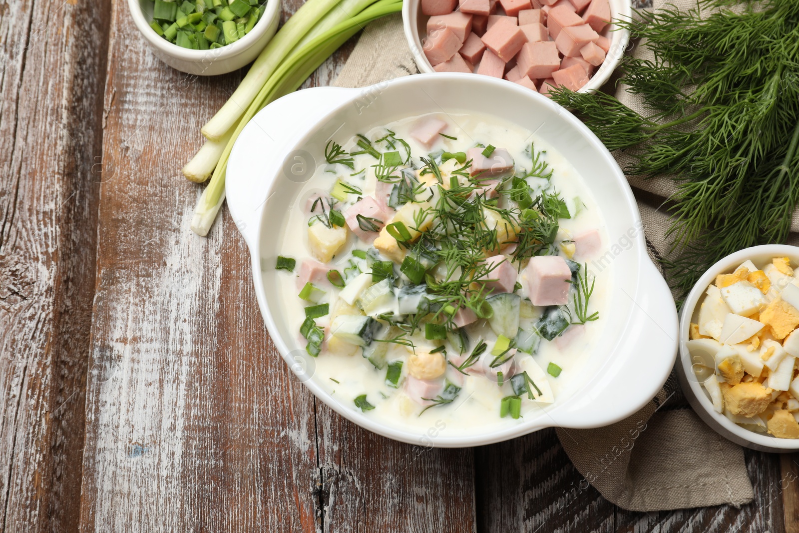 Photo of Delicious okroshka soup in bowl and ingredients on wooden table, flat lay. Space for text