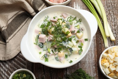 Photo of Delicious okroshka soup in bowl and ingredients on wooden table, flat lay