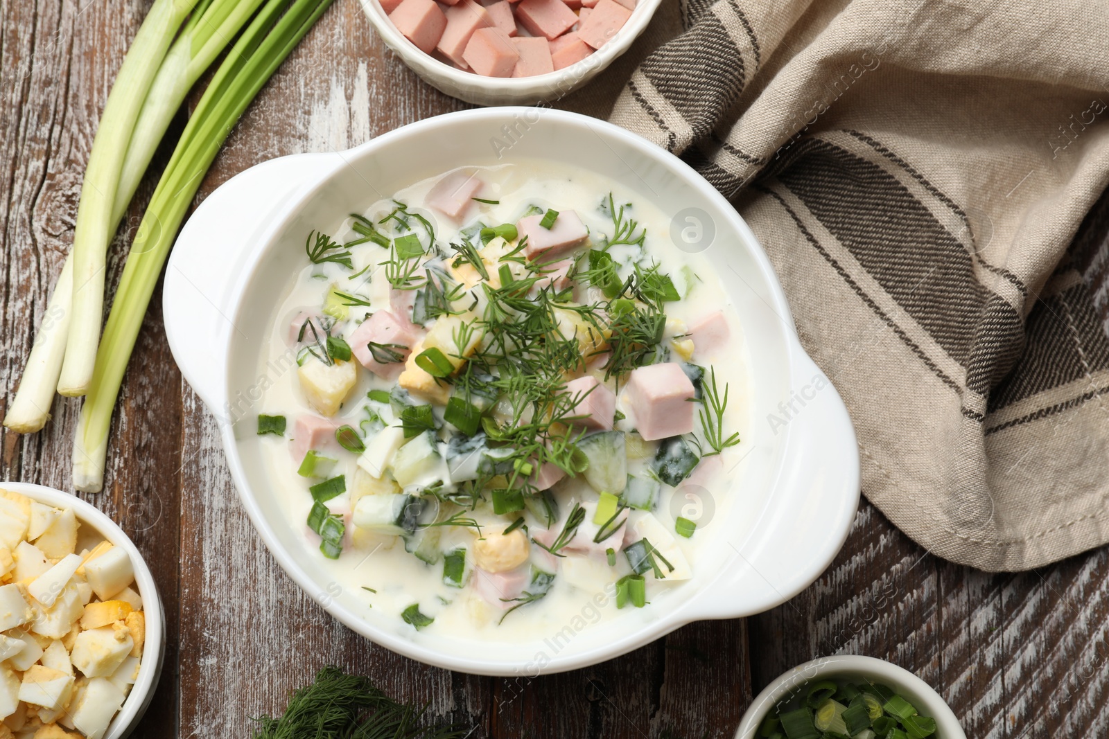 Photo of Delicious okroshka soup in bowl and ingredients on wooden table, flat lay