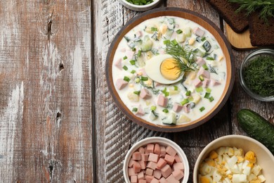 Photo of Delicious okroshka soup with kefir in bowl and ingredients on wooden table, flat lay. Space for text