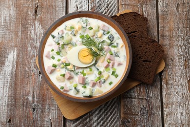 Photo of Delicious okroshka soup with kefir in bowl and bread on wooden table, top view