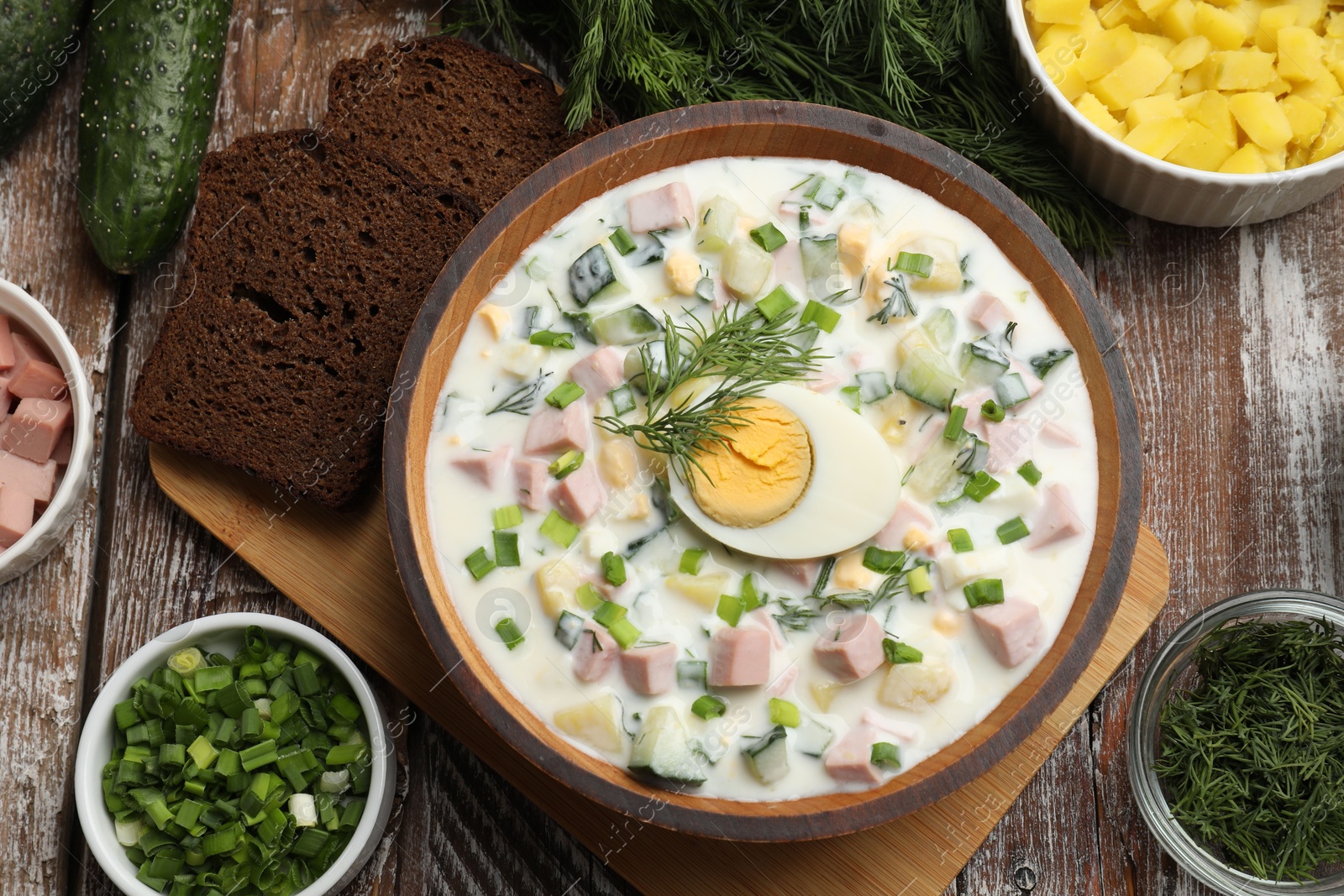 Photo of Delicious okroshka soup with kefir in bowl and ingredients on wooden table, flat lay