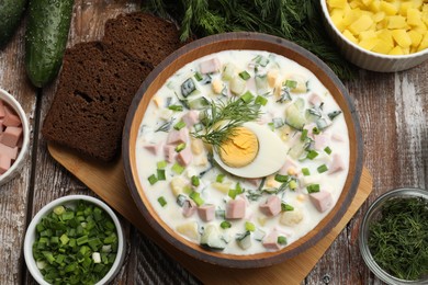 Photo of Delicious okroshka soup with kefir in bowl and ingredients on wooden table, flat lay