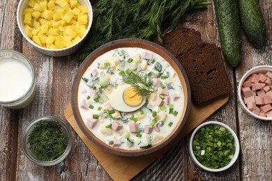 Photo of Delicious okroshka soup with kefir in bowl and ingredients on wooden table, flat lay