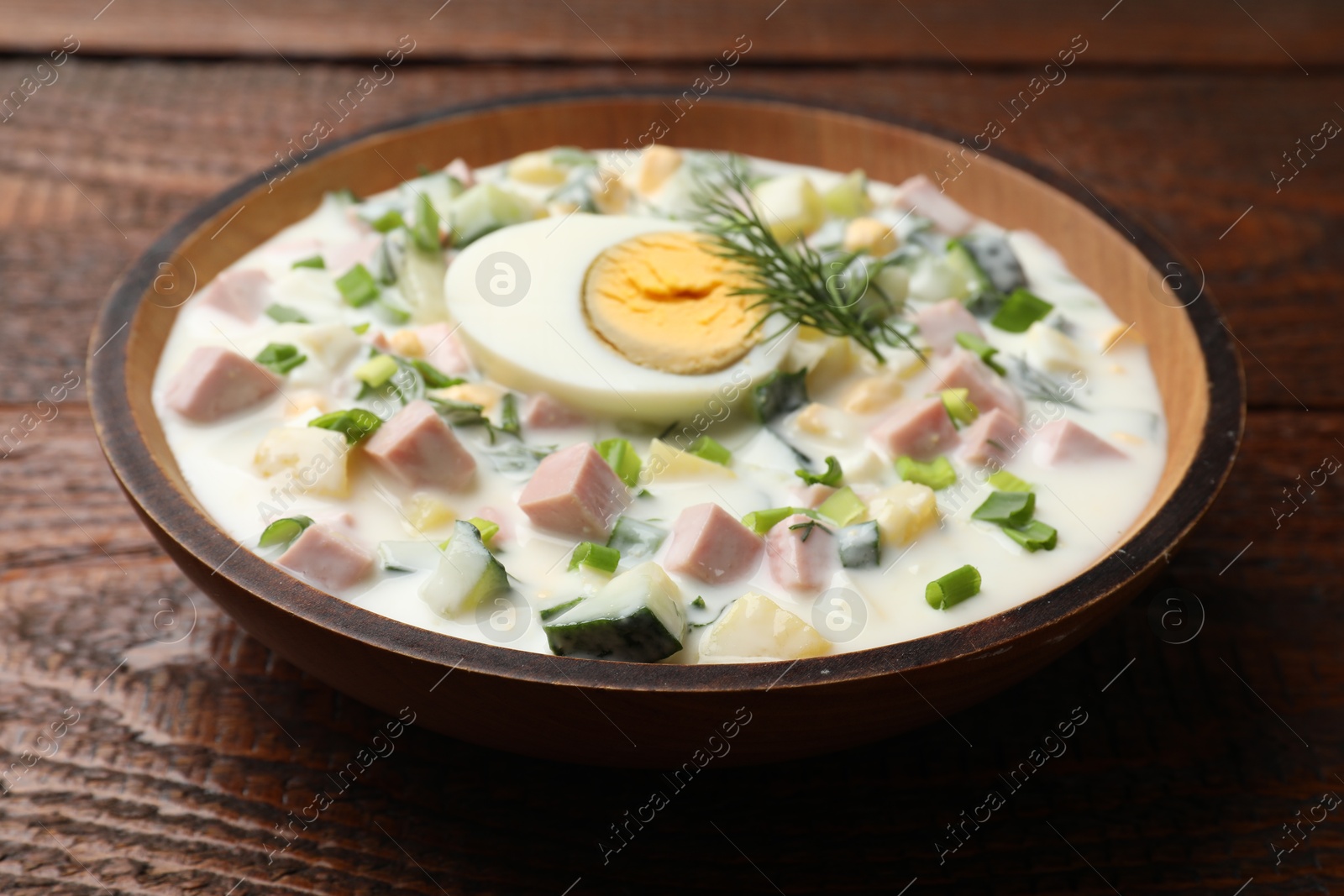 Photo of Delicious okroshka soup with kefir in bowl on wooden table, closeup