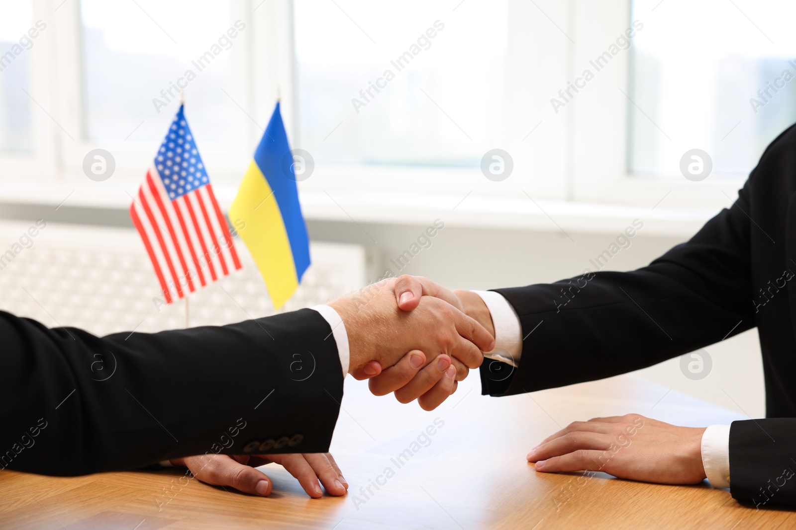 Photo of Diplomats shaking hands during meeting at wooden table indoors, closeup