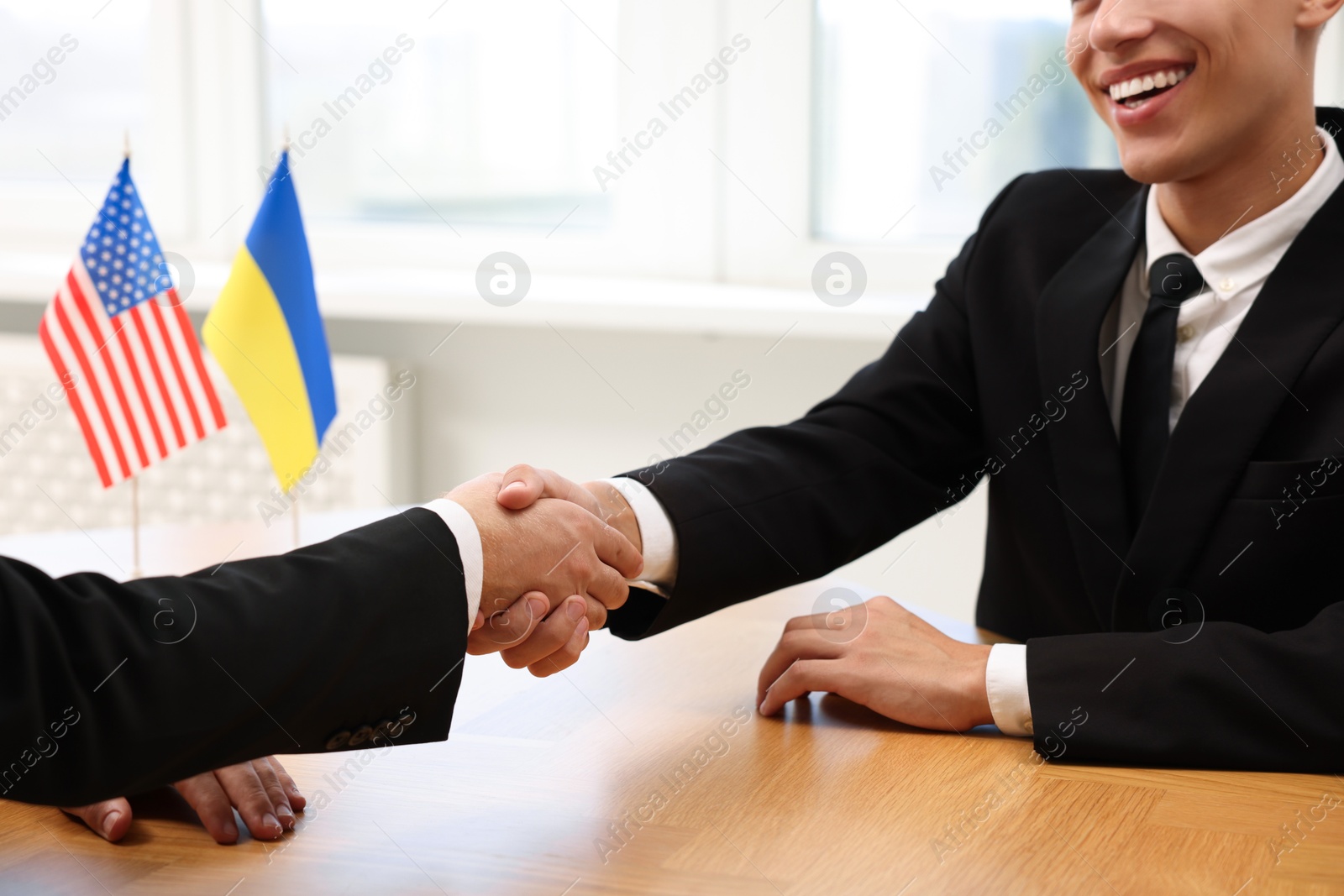 Photo of Diplomats shaking hands during meeting at wooden table indoors, closeup