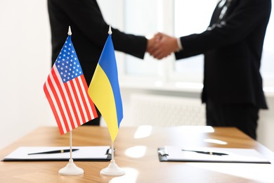 Photo of Diplomats shaking hands during meeting indoors, focus on flags of USA and Ukraine