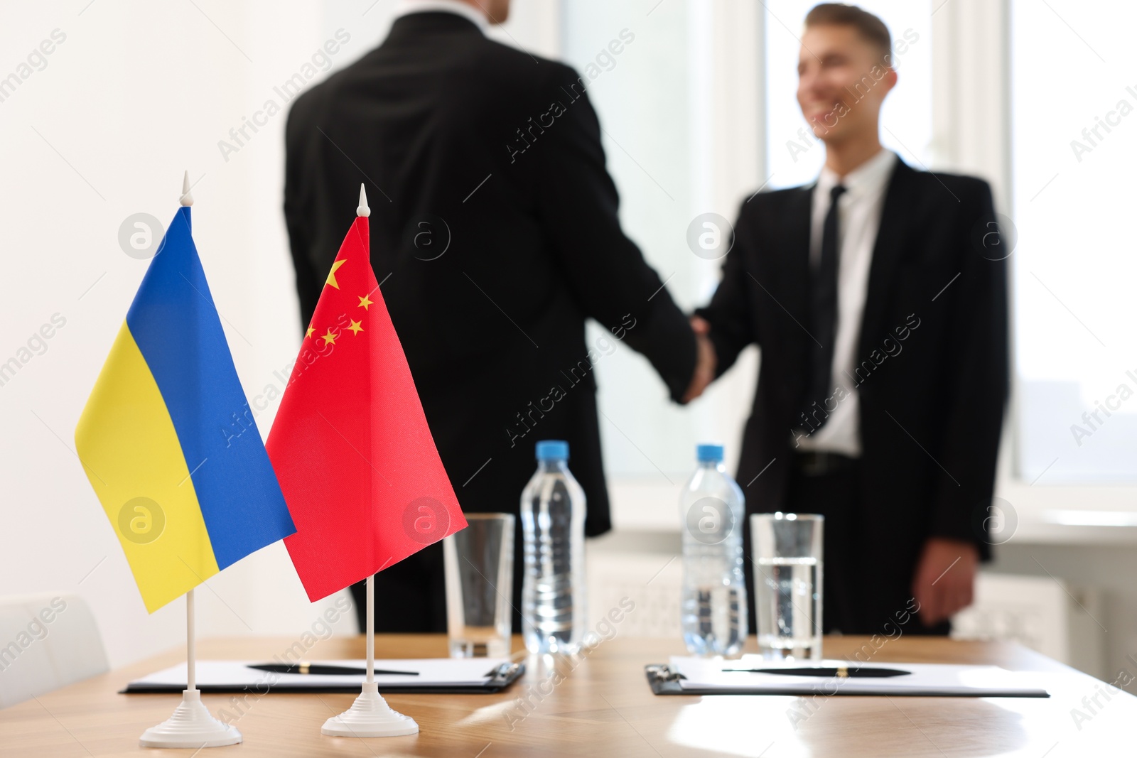 Photo of Diplomats shaking hands during meeting indoors, focus on flags of Ukraine and China