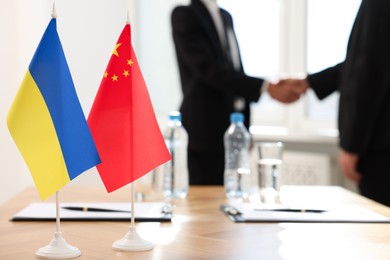 Diplomats shaking hands during meeting indoors, focus on flags of Ukraine and China