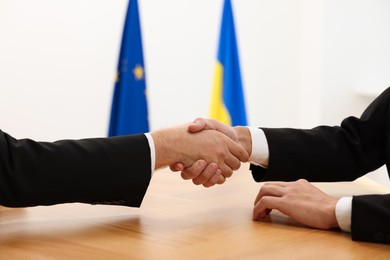 Photo of Diplomats shaking hands during meeting at wooden table indoors, closeup