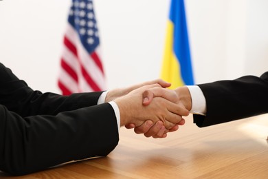 Photo of Diplomats shaking hands during meeting at wooden table indoors, closeup