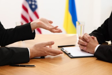 Photo of Diplomats negotiating during meeting at wooden table indoors, closeup