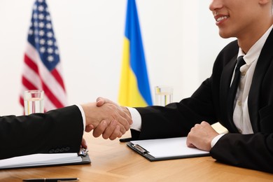 Photo of Diplomats shaking hands during meeting at wooden table indoors, closeup