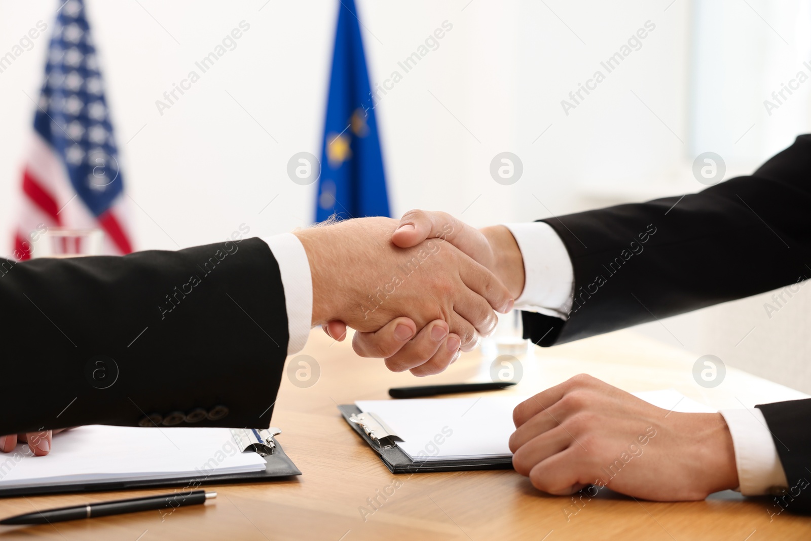 Photo of Diplomats shaking hands during meeting at wooden table indoors, closeup