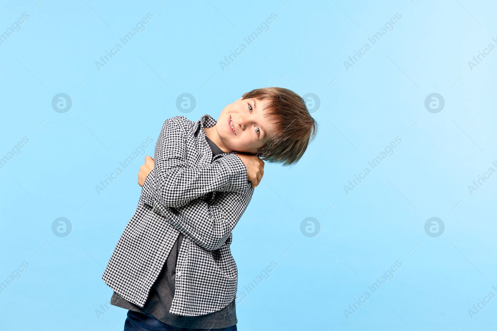 Photo of Cute little boy hugging himself on light blue background, space for text