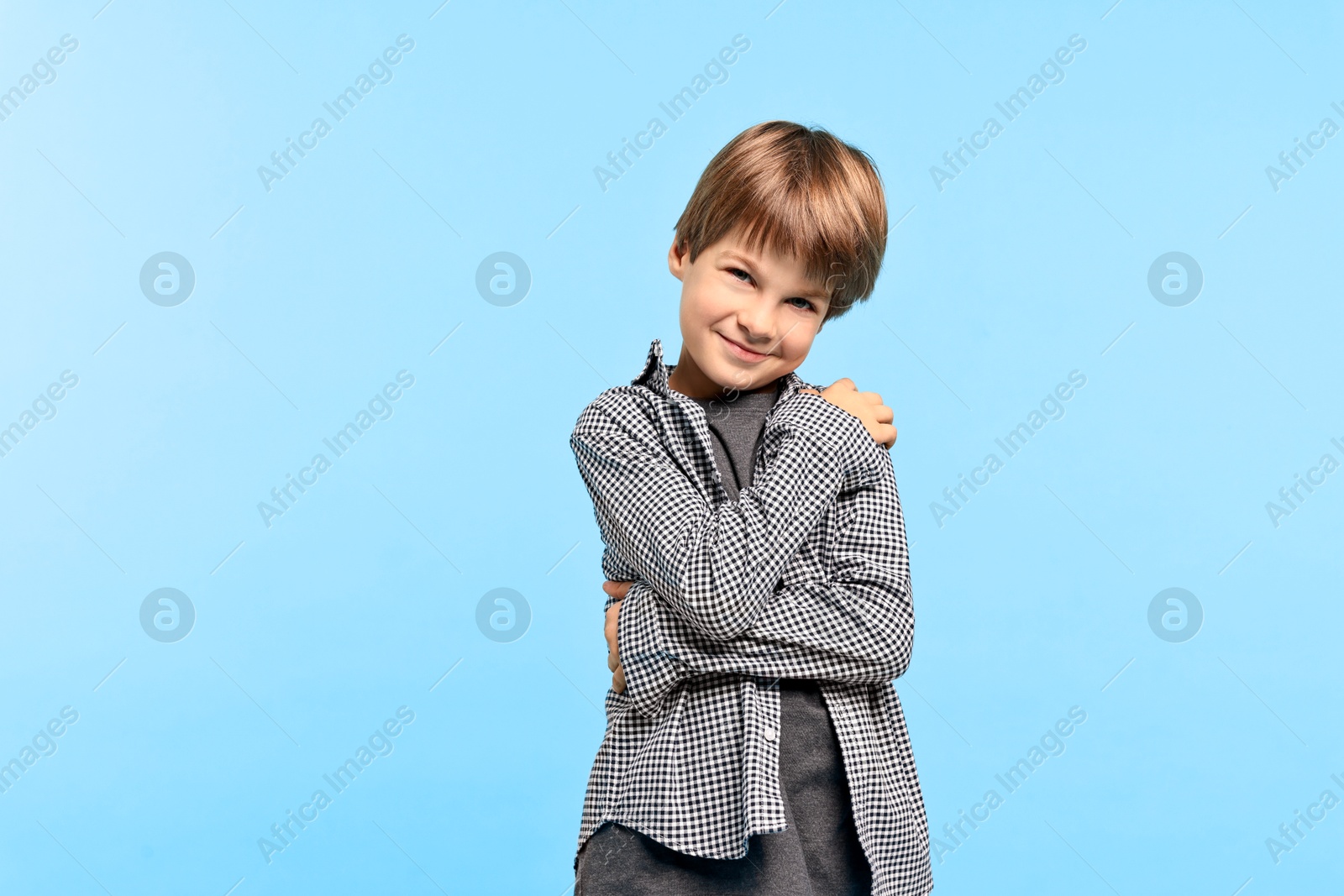 Photo of Cute little boy hugging himself on light blue background