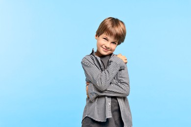 Photo of Cute little boy hugging himself on light blue background