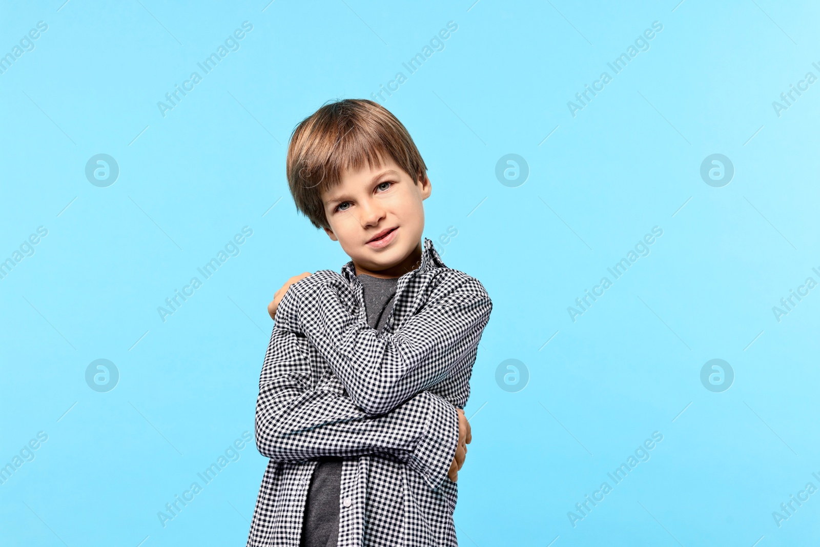 Photo of Cute little boy hugging himself on light blue background