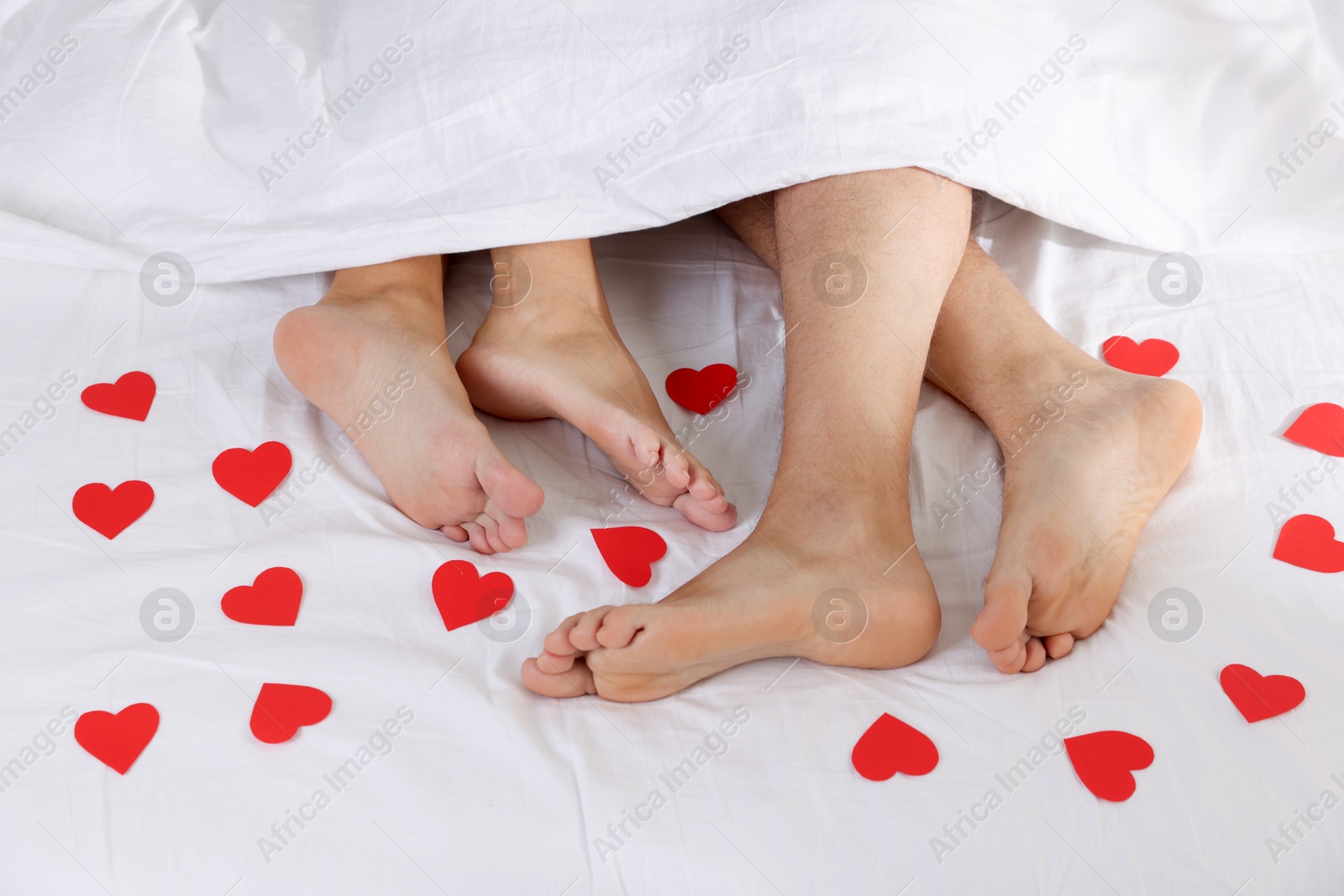 Photo of Couple lying in bed with red paper hearts, top view