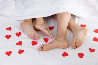 Photo of Couple lying in bed with red paper hearts, top view