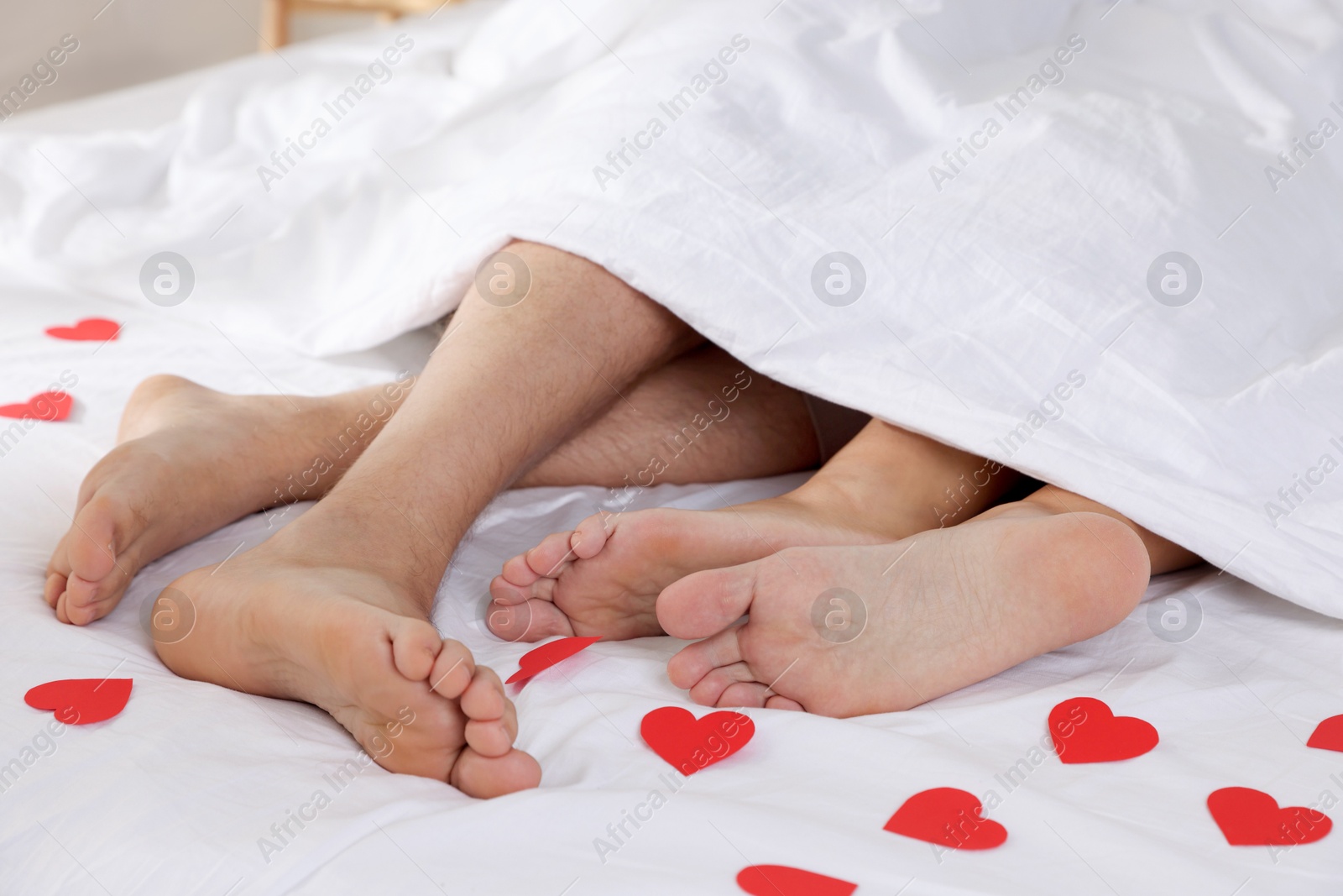 Photo of Couple lying in bed with red paper hearts, closeup