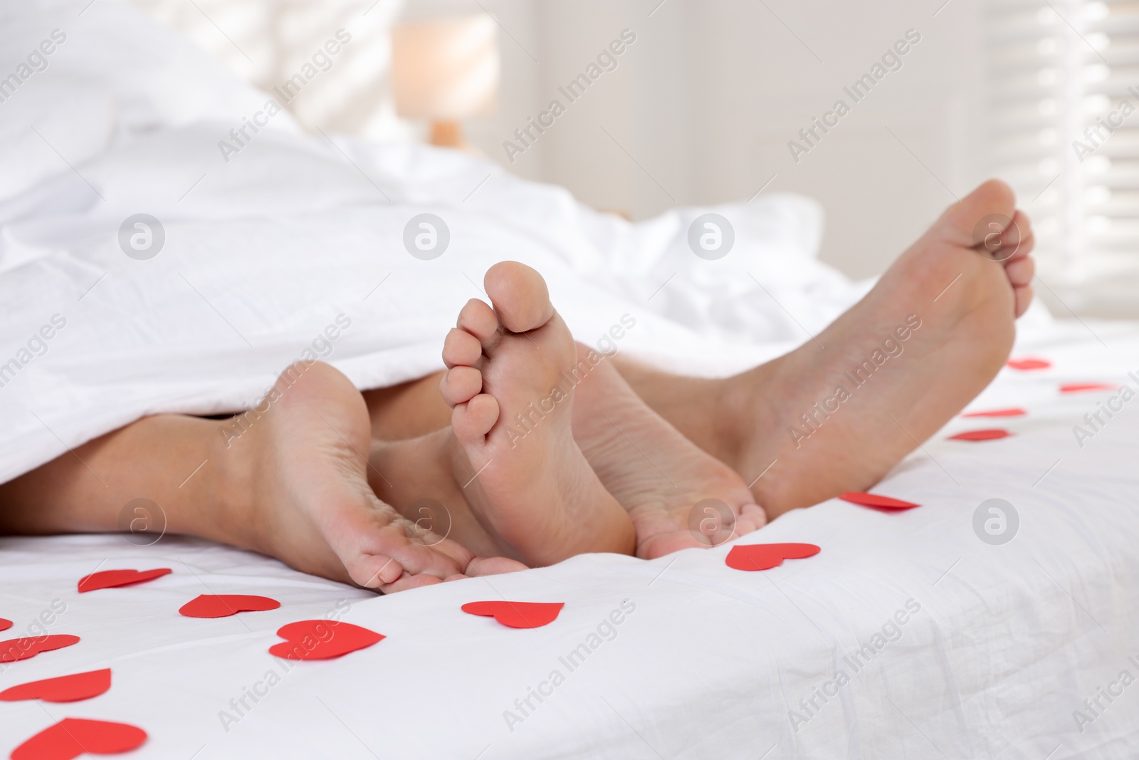 Photo of Couple lying in bed with red paper hearts, closeup