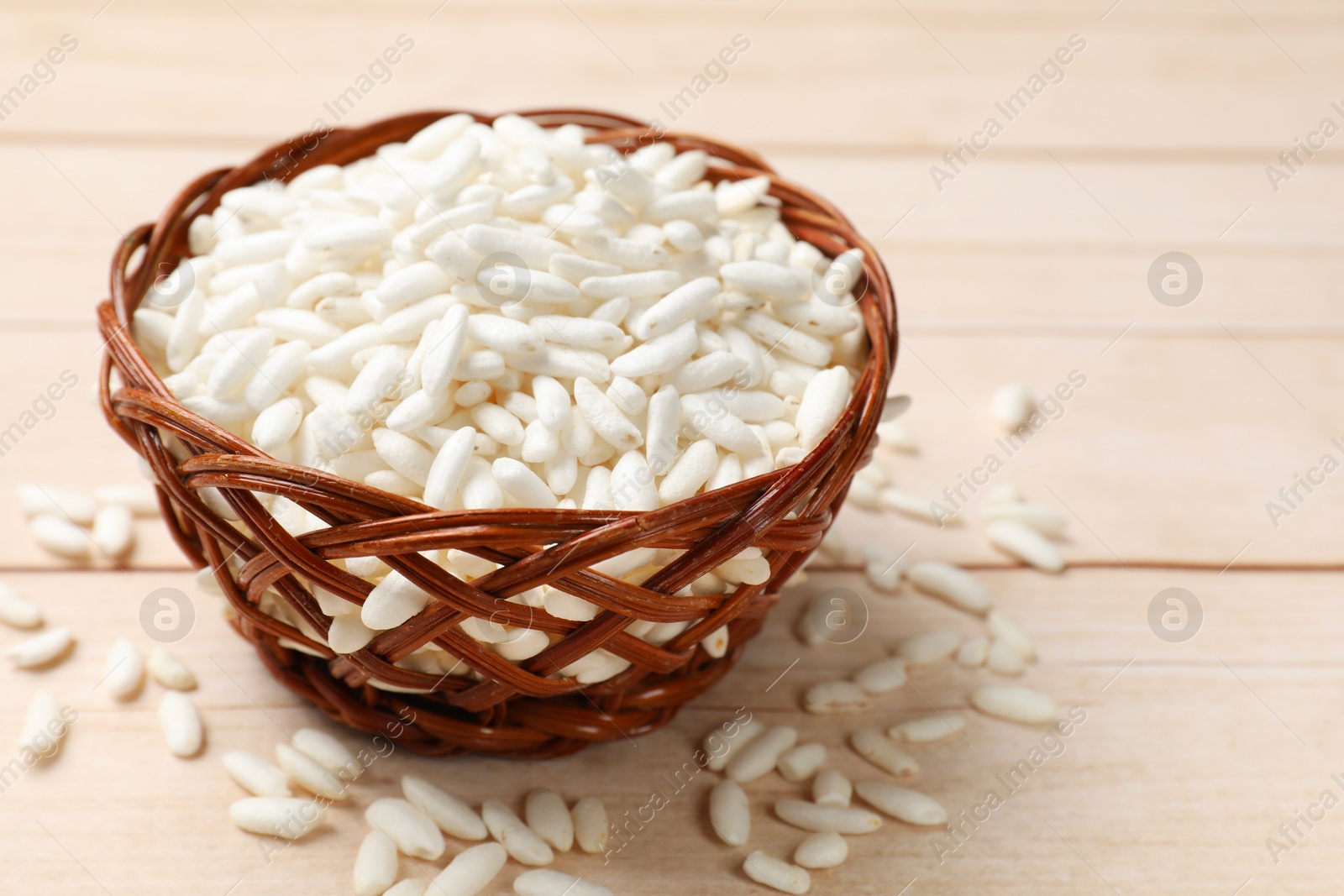 Photo of Puffed rice in wicker basket on wooden table, closeup. Space for text