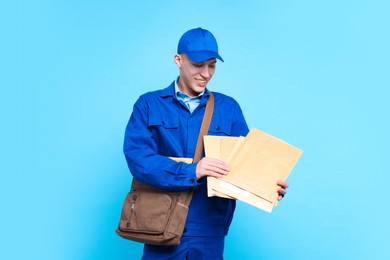 Photo of Happy postman with bag and envelopes on light blue background