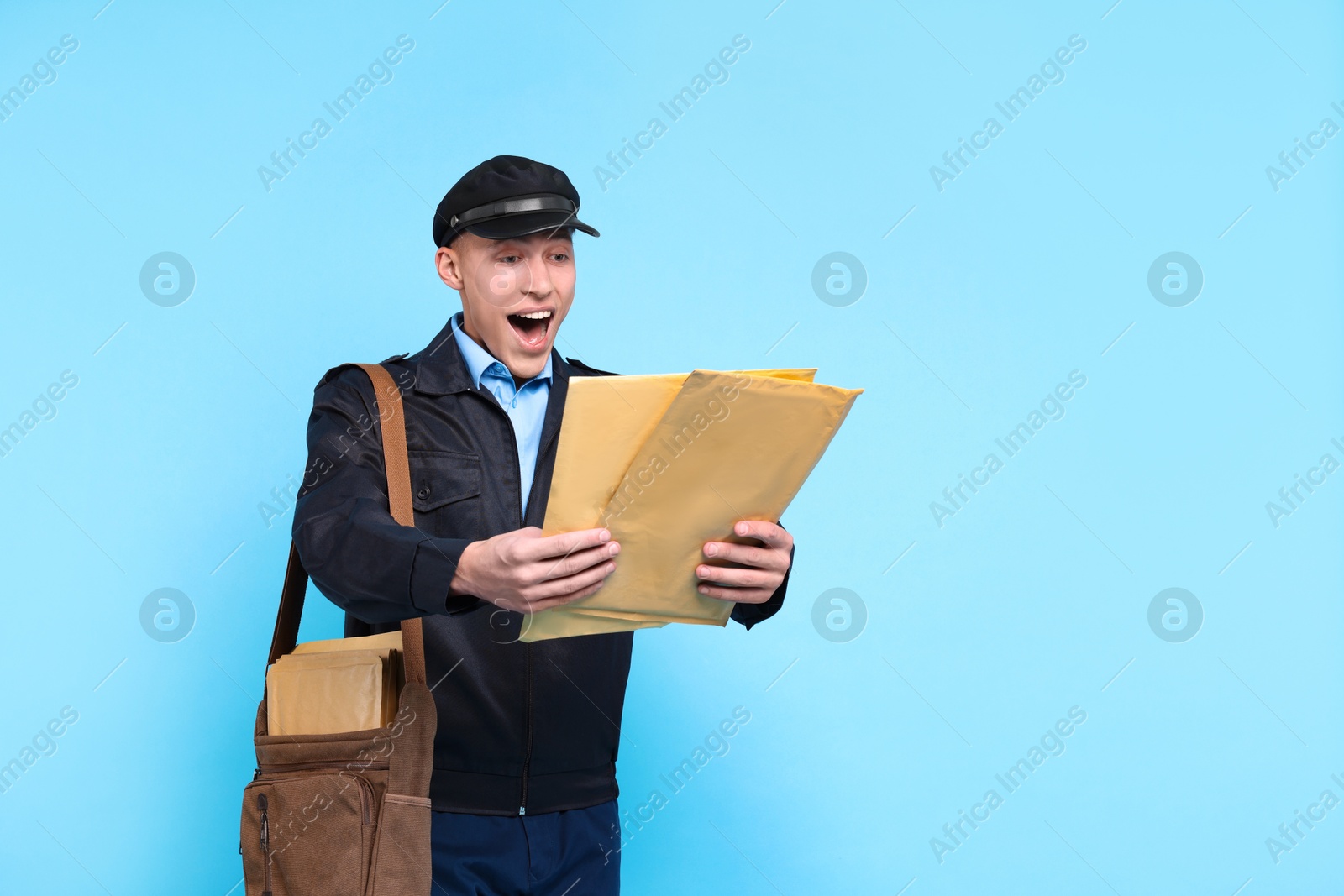 Photo of Emotional postman with bag and envelopes on light blue background. Space for text