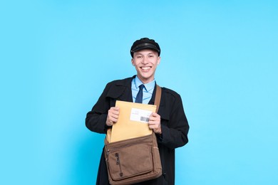 Photo of Happy postman with bag and envelopes on light blue background