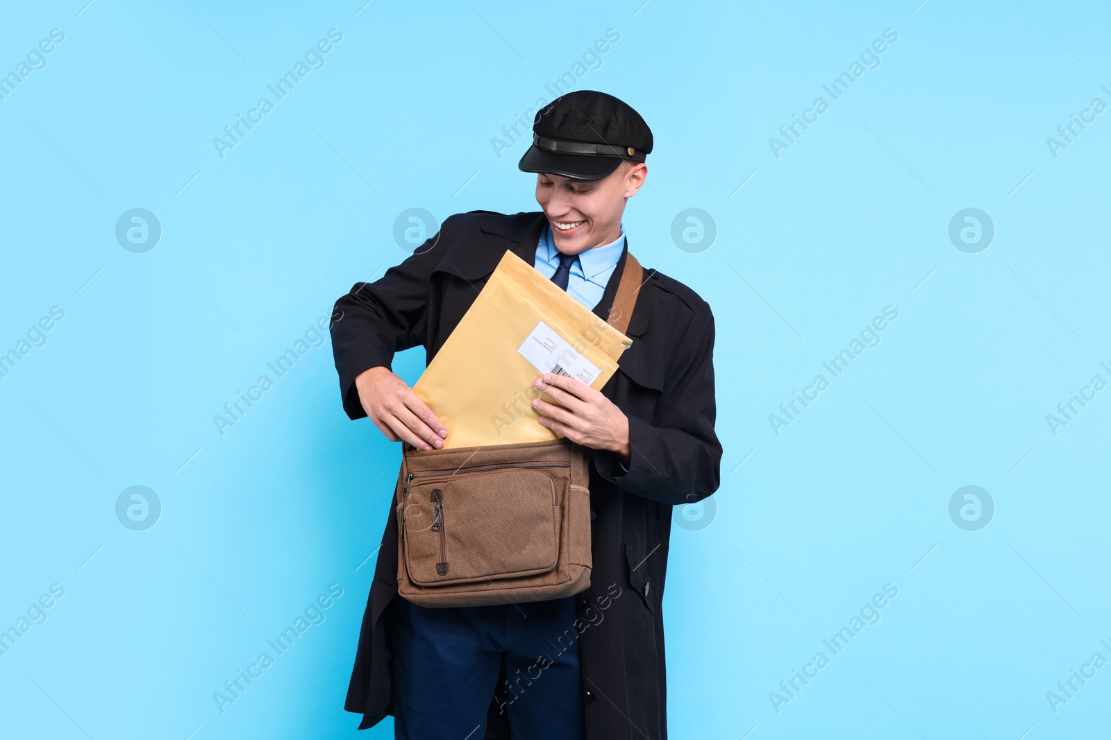 Photo of Happy postman with bag and envelopes on light blue background. Space for text