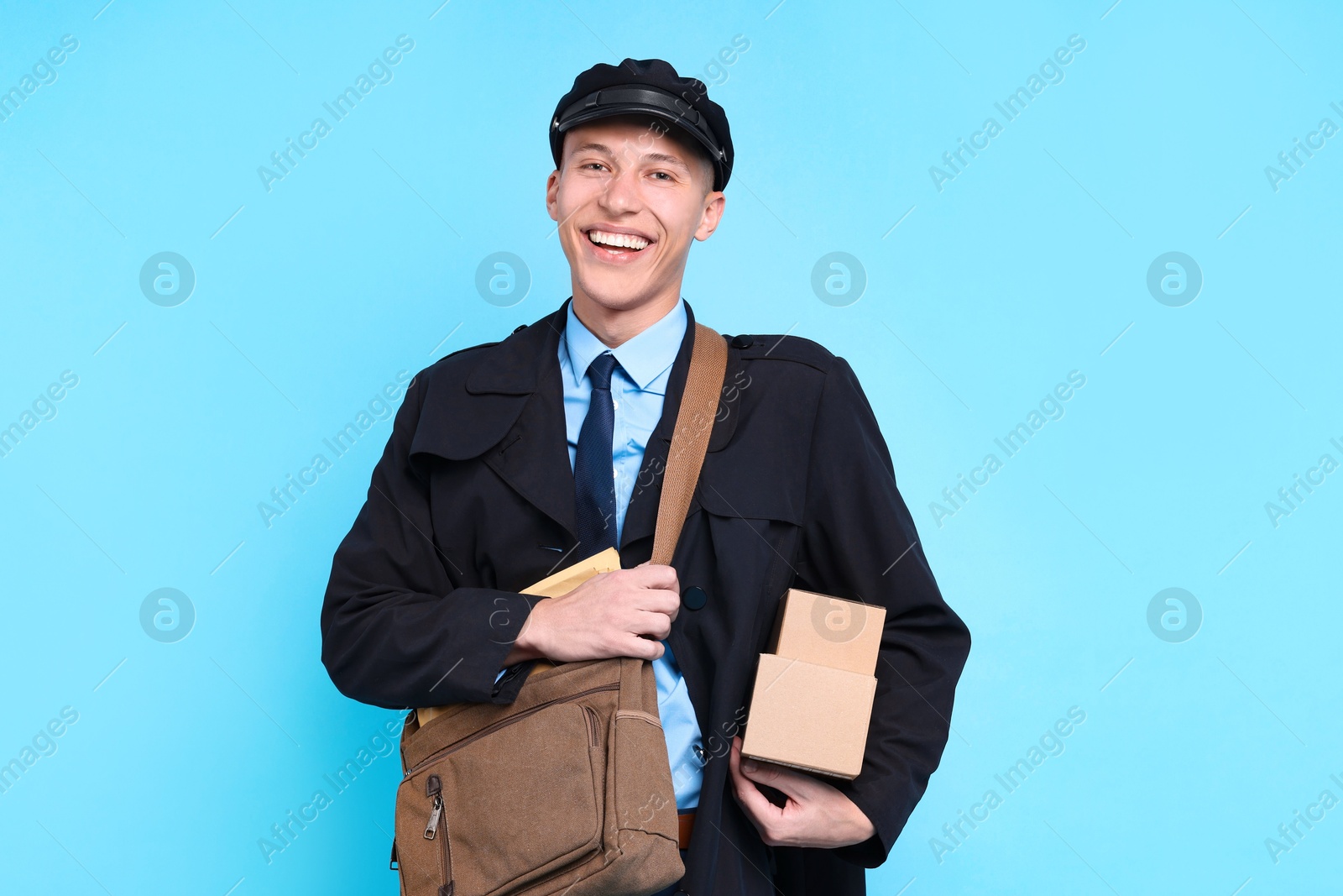 Photo of Happy postman with bag and parcels on light blue background