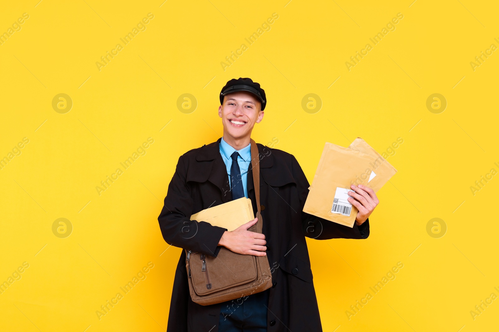 Photo of Happy postman with bag and envelopes on yellow background. Space for text