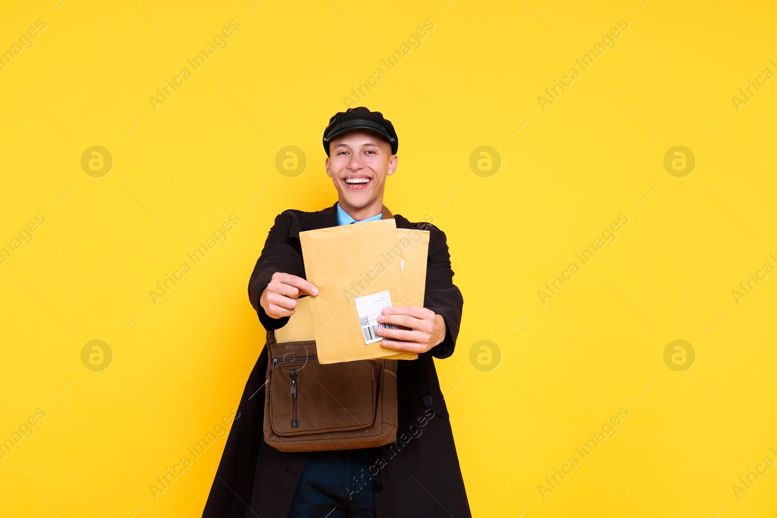 Photo of Happy postman with bag giving envelopes on yellow background