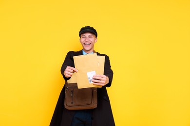 Photo of Happy postman with bag giving envelopes on yellow background