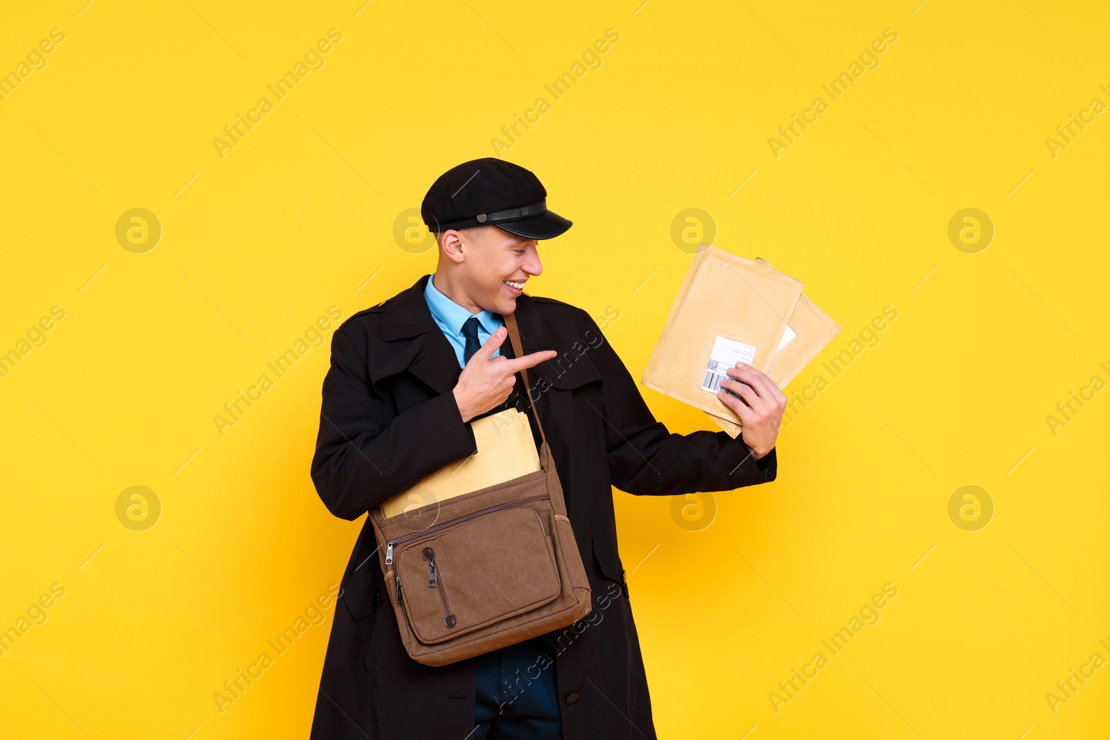 Photo of Happy postman with bag pointing at envelopes on yellow background