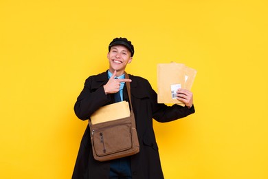 Photo of Happy postman with bag pointing at envelopes on yellow background