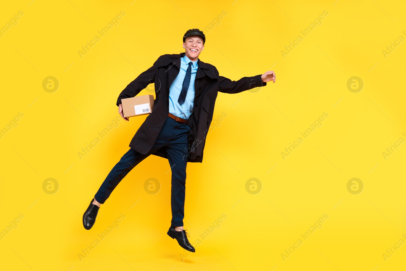 Photo of Happy postman with parcel jumping on yellow background